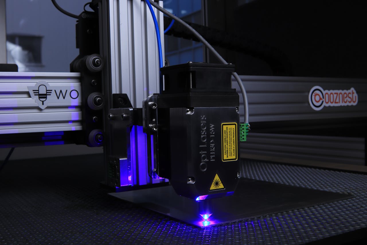 gallery-5 Close-up of a high-tech laser cutter operating indoors with blue lighting.